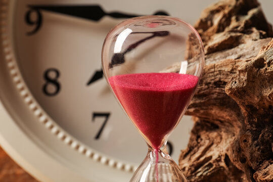 Close-up of hourglass with red sand and clock background