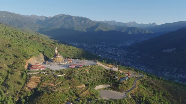 Aerial view of the massive Buddha Dordenma statue perched on a mountain ridge overlooking the Thimphu valley with lush green slopes and distant peaks in Thimphu, Thimphu, Bhutan.
