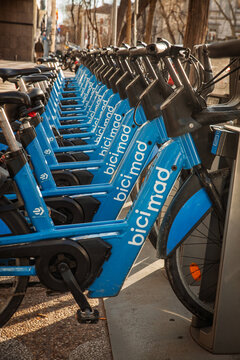 MADRID, SPAIN - FEBRUARY 22, 2026: BiciMAD rental bicycles lined up at a docking station in Madrid, Spain, blue shared electric bikes, bicimad is the city's public bicycle-sharing system of Madrid.