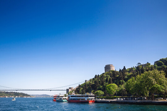 Panoramic view of Halil Pasha Tower at Rumeli Fortress, also called Rumelihisari, on the Bosphorus in Istanbul, Turkey, with waterfront greenery, passenger boats and Ottoman fortifications by the stra