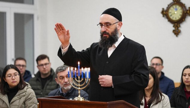 Rabbi conducting a Hanukkah ceremony with menorah and blue candles at a synagogue with members