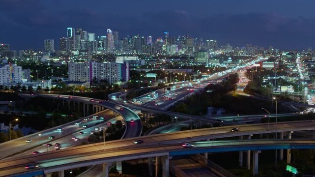 Miami night traffic cityscape aerial drone view of busy interstate 95 highway and big elevated intersection toward downtown urban infrastructure in 4K Ultra HD footage.
