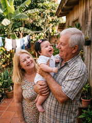 Fototapeta premium Grandparents holding laughing baby outdoors