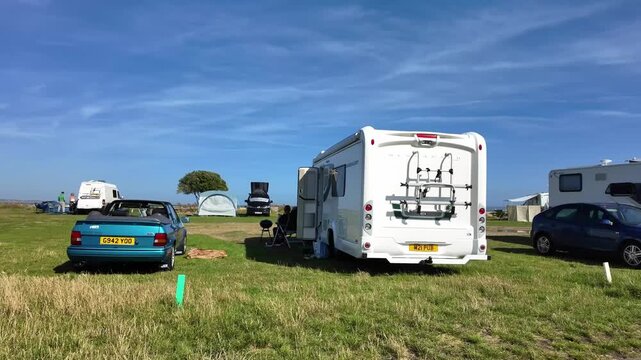 Hampshire England UK. 12.06.2026. Video. Motorhomes and cars are parked on a grassy field under a bright blue sky with wispy clouds, suggesting a pleasant day for outdoor recreation