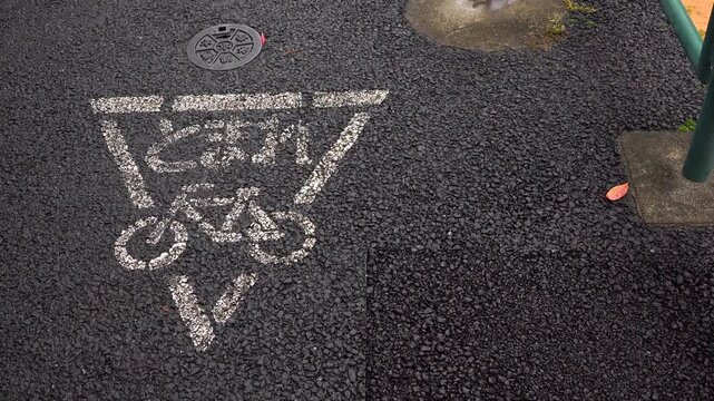 Left-positioned close-up of bicycle stop pavement marking on wet sidewalk in Japan on a light rainy morning