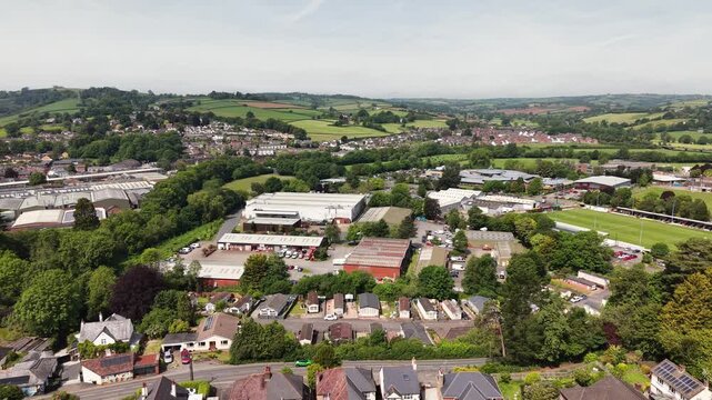 Cinematic aerial drone footage showcasing the historic market town of Tiverton in Devon, England. The flight captures the town, residential neighborhoods, architecture, surrounding countryside