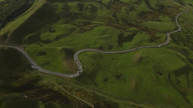 Aerial view of the winding road through the lush green hills of Mam Tor in Castleton, England, United Kingdom.