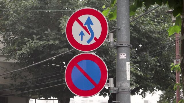 Close-up of Japanese no overtaking and no parking road signs on a pole in light rain during early morning