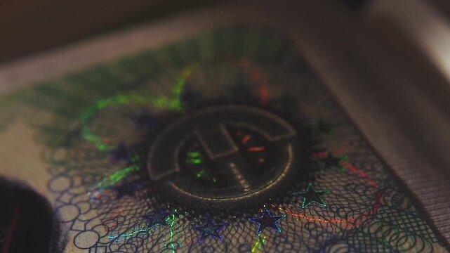 A close-up of the illuminated holographic emblem of the EU Schengen visa. The iridescent multicolor security hologram of the Schengen visa of the European Union countries. 4k slow motion video 60 fps.
