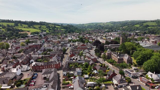 Cinematic aerial drone footage showcasing the historic market town of Tiverton in Devon, England. The flight captures the town, residential neighborhoods, architecture, surrounding countryside