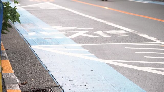 Wet Tokyo bus stop road marking with passing vehicles on a light rainy early morning