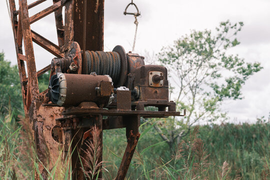 Derelict industrial crane with rusty winch in overgrown field