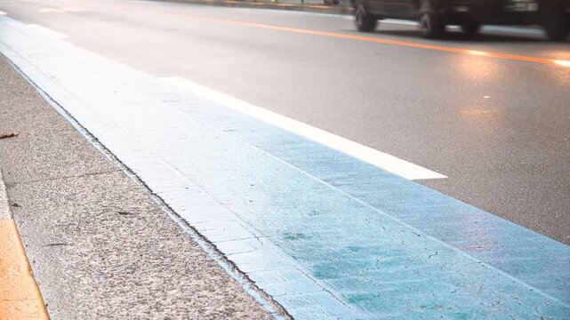 Low angle view of wet blue bicycle lane beside roadway with passing car in opposite lane on a rainy Tokyo morning