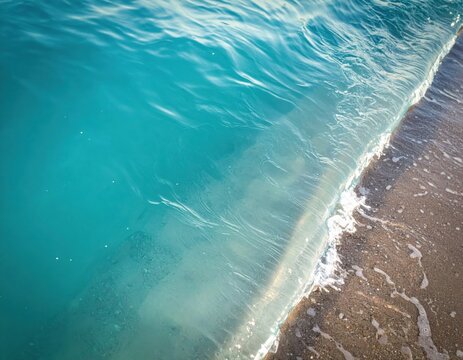 Turquoise sea water gently lapping against a weathered concrete pier edge. Clear ocean waves hitting a stone seawall, coastal marine environment, summer travel.