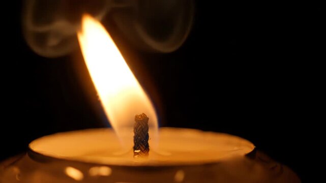 Cinematic extreme close up of a single candle flame flickering softly against a pitch black background with warm glowing light