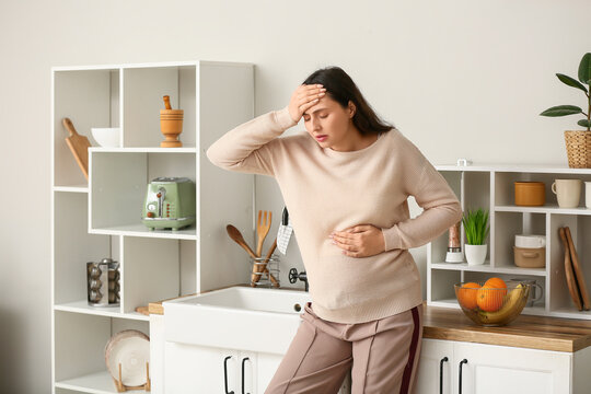 Young pregnant woman suffering from toxicosis near sink in kitchen