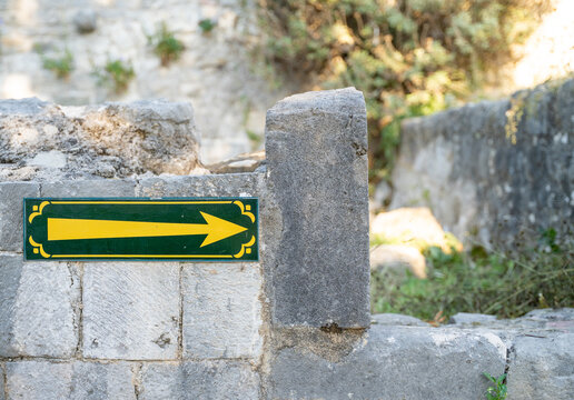 Yellow directional arrow sign attached to an ancient stone wall in an outdoor nature setting, wayfinding concept