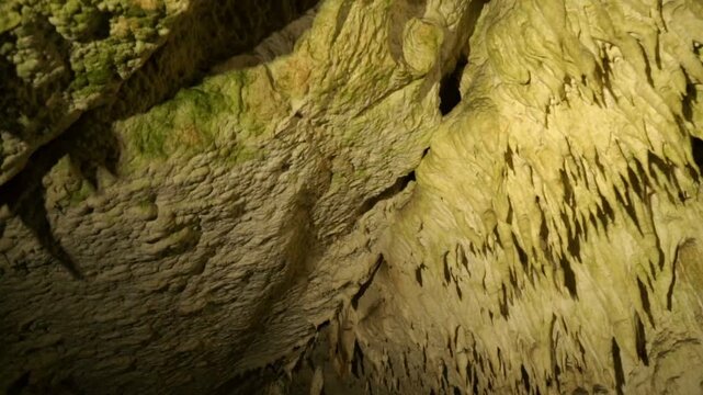 Speleology cave exploration of deep underground cavern with geological mineral stalactites illuminated by flashlight beam in 4K Ultra HD footage.
