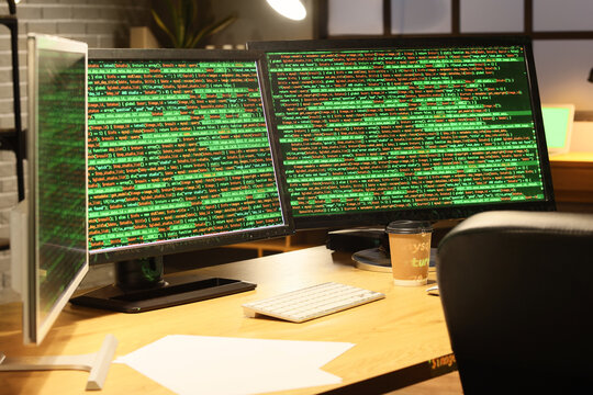 Computer monitors with programming code on table in dark office at night