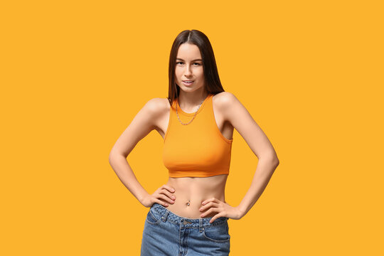 Beautiful young woman with piercing navel on yellow background