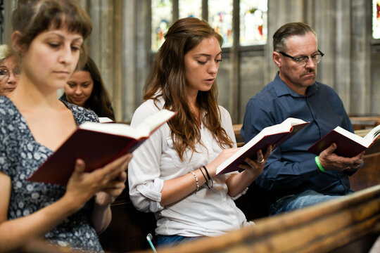People sitting in a church pew, reading books during a service.