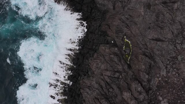 Aerial view of the rugged volcanic coastline at Miradouro da Ponta do Queimado with powerful waves crashing against dark basalt cliffs in Serreta, Acores, Portugal.