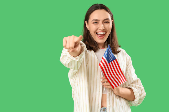 Laughing young woman with USA flag pointing at viewer on green background. Accusation concept
