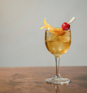 An Old Fashioned cocktail served in a crystal glass with ice, an orange peel garnish, and a maraschino cherry on a pick By Camila