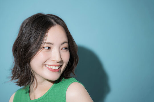 背景がブルーグリーンで洋服のビタミンカラーの元気いっぱいの美容やビューティーイメージのかわいい女性　クローズアップ