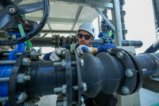 Engineer maintenance hvac cooling tower technician industrial pipe repair safety at work adjusts flange and valve on large pipeline with hardhat and glove for reliable operation and steady service
