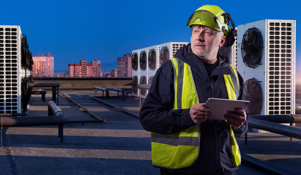 HVAC maintenance, technician checks rooftop air conditioning units with tablet during building climate system inspection at dusk