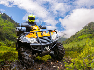 Obraz premium ATV off-road riding expedition navigates muddy mountain trail with quad bike in rugged terrain and scenic valley landscape