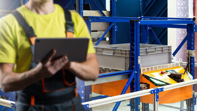 Warehouse logistics technician monitors automated storage system using tablet in distribution center with shelving racks and conveyor equipment