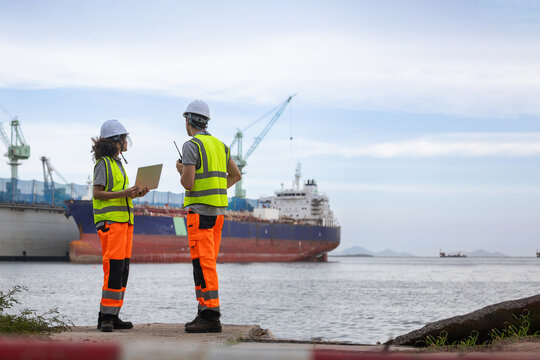 Industrial engineers using laptop and radio at shipping port, Professional logistics team working at commercial cargo terminal, Marine engineers in safety gear inspecting shipping vessel at harbor