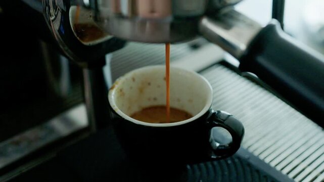 4K Pouring coffee stream from professional machine in cup. Barista man making double espresso, using filter holder. Flowing fresh ground coffee. Drinking roasted black coffee in the morning.