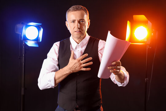 Mature actor reading film script on dark background