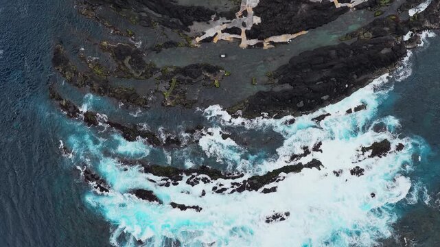 Aerial view of Biscoitos volcanic rock pools with crashing waves and dark basalt formations along the coastline in Biscoitos, Azores, Portugal.