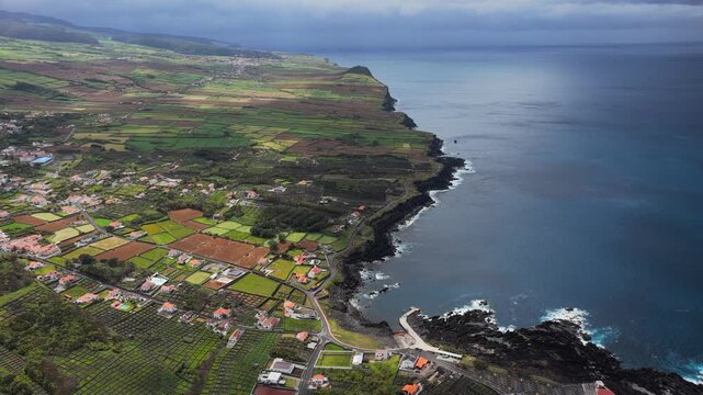 Aerial view of the coastal landscape of Biscoitos featuring lush green agricultural fields, volcanic rock formations, and the Atlantic Ocean in Biscoitos, Azores, Portugal.