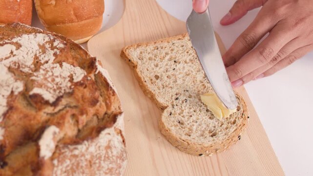 Spreading Butter on Multigrain Bread with Assorted Bakery Loaves
