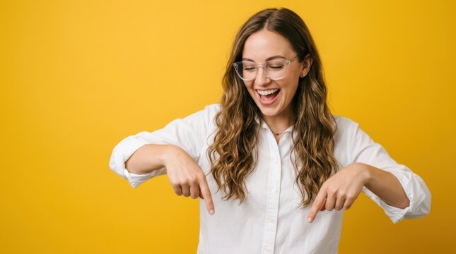 Young woman with glasses pointing down against a yellow background