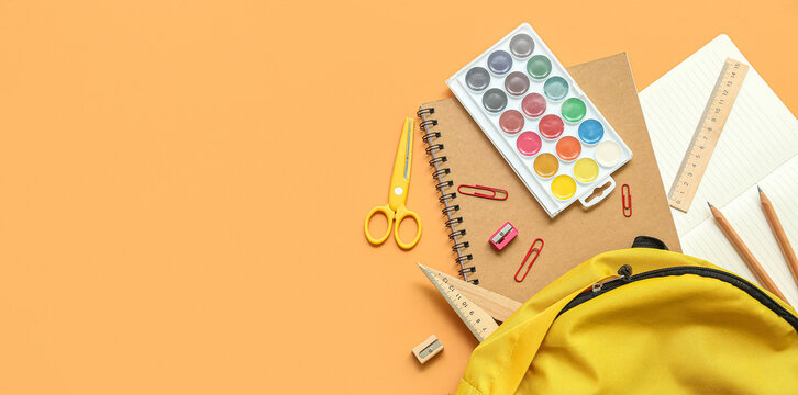 Flat lay of school supplies with yellow backpack on orange background