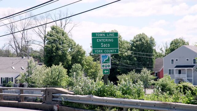 Green town line road sign welcoming drivers entering Saco York County Maine on a sunny summer day