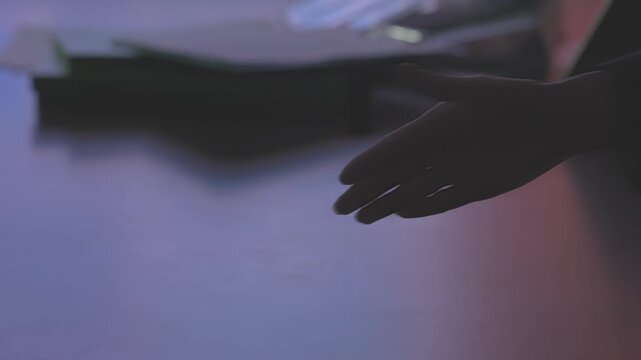 A close-up of a person's hands resting on a dark reflective surface in a calm and minimal indoor setting.