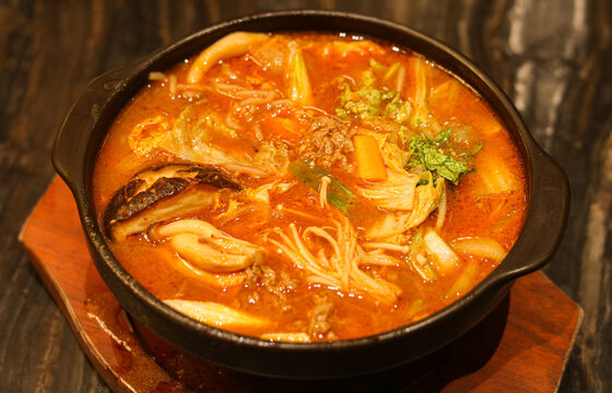 Closeup of spicy beef nabe hotpot featuring vegetables and tofu cubes in a bubbling rich red broth.