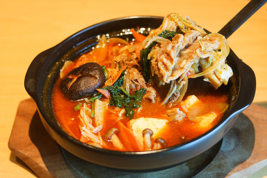 Eating spicy beef nabe hotpot featuring vegetables and tofu cubes in a bubbling rich red broth.