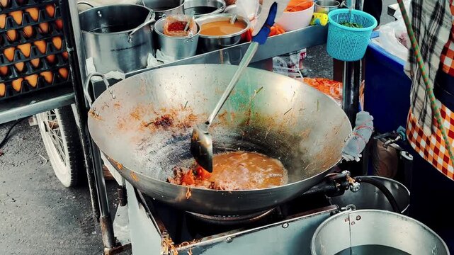 Close up of chef stirring and frying noodles with bean sprouts in a giant wok, authentic Thai street food.