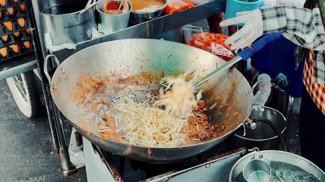 Close up of chef stirring and frying noodles with bean sprouts in a giant wok, authentic Thai street food.