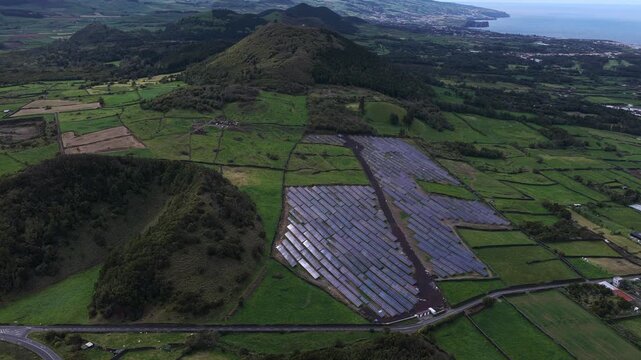 Aerial view of solar farm panels arranged in rows within a lush green volcanic landscape near Rabo de Peixe, Acores, Portugal.