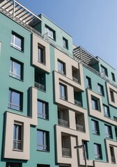 Obraz premium Modern Teal and Beige Apartment Building Facade with Geometric Design and Balconies under Clear Blue Sky