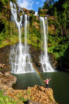 Young female tourist enjoying a beautiful waterfall with a rainbow at Tad Gneuang in Southern Laos